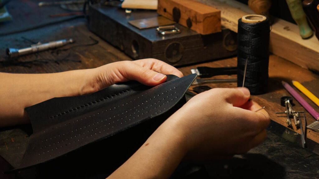 A craftsman working leather by hand in a workshop, representing the individual artisan behind each blind stamp