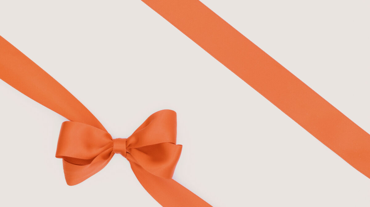 Hermès orange gift box with satin ribbon bow, editorial cream and gold presentation style